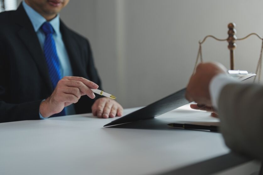 Lawyer holding a pen and pointing at a document during a meeting with a client, with scales of justice in the background symbolizing law and order, legal advice, and justice