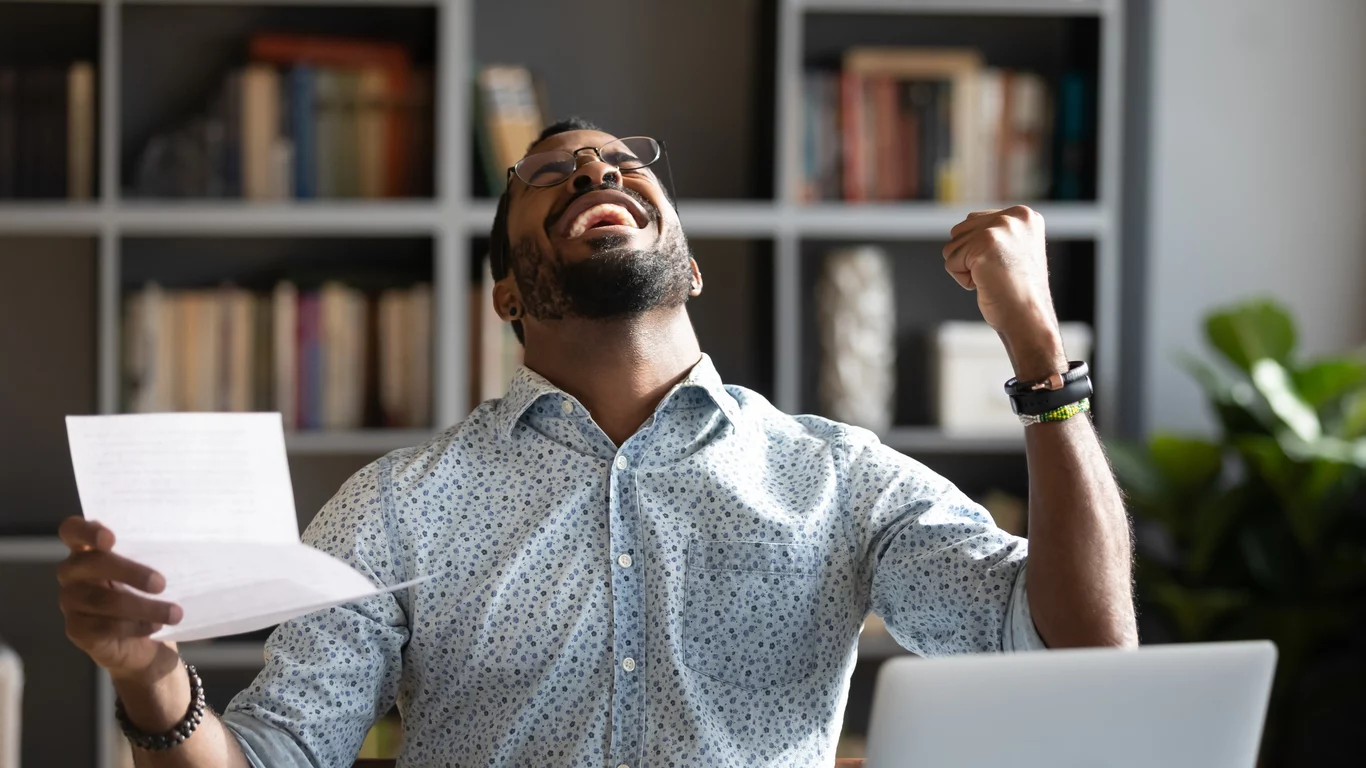 Overjoyed young man in glasses holding paper in hands, celebrating the IRS 1.2 Billion IRS tax break