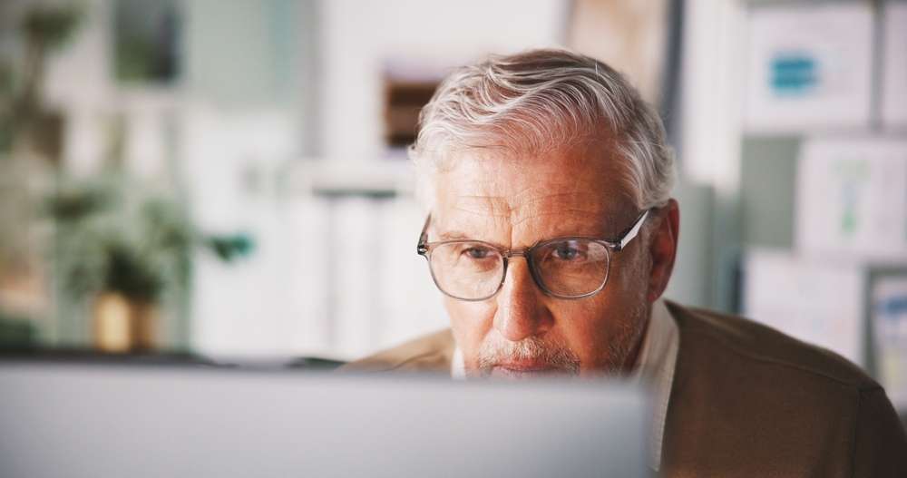 Mature, computer and reading with business man in office for seo research, blog traffic and review. Search volume report, planning and engagement ranking with person in media agency for kpi insight